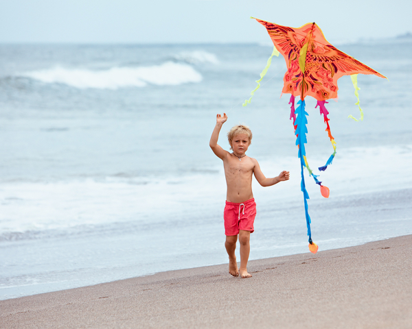 Boy running with flying kite along surf edge